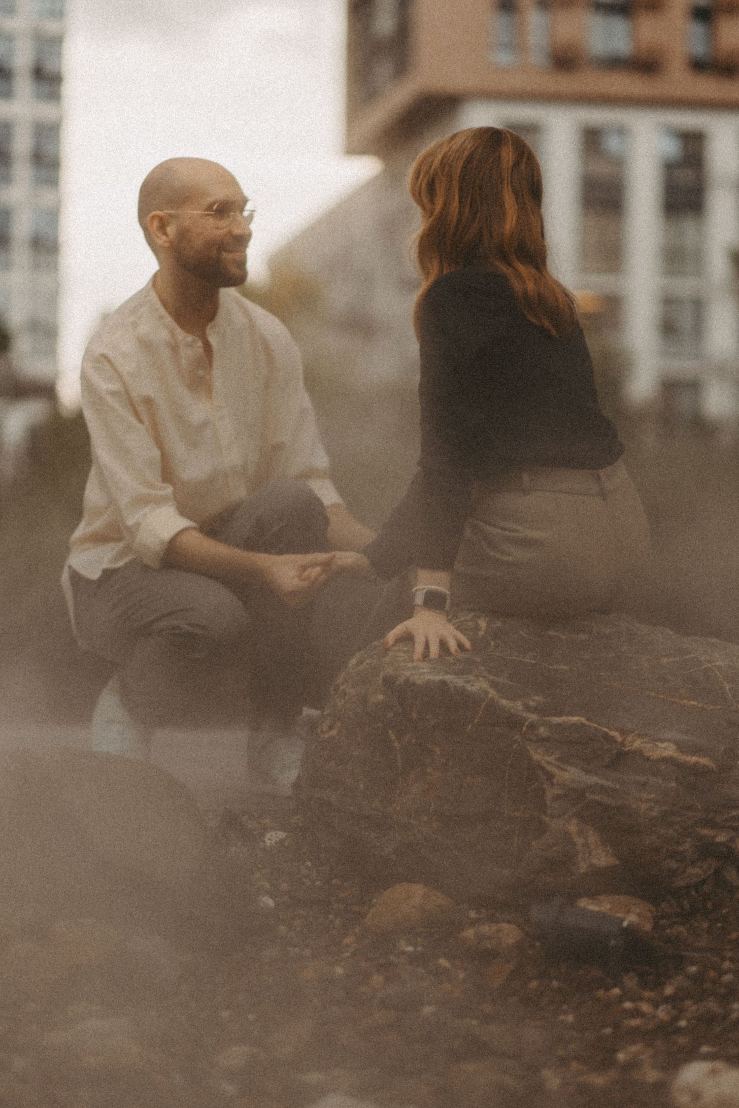 Two people share a conversation while sitting on rocks in an urban setting.