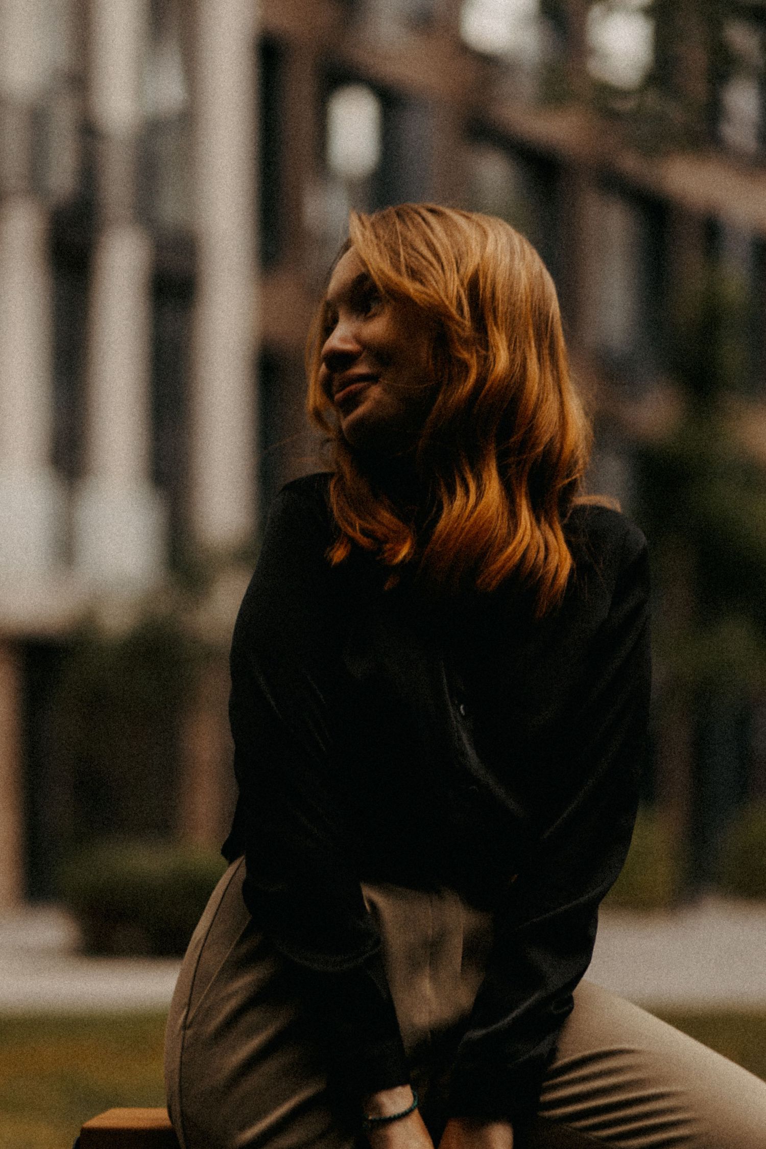 Person in black sweater sits thoughtfully against urban backdrop.