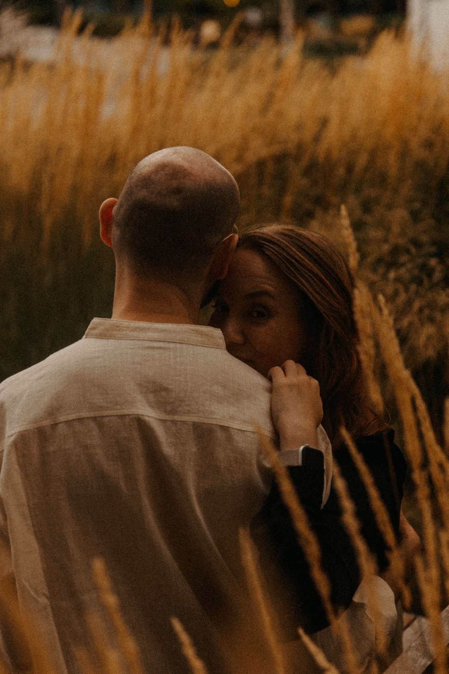 A romantic embrace captured in golden hour light among tall grass.
