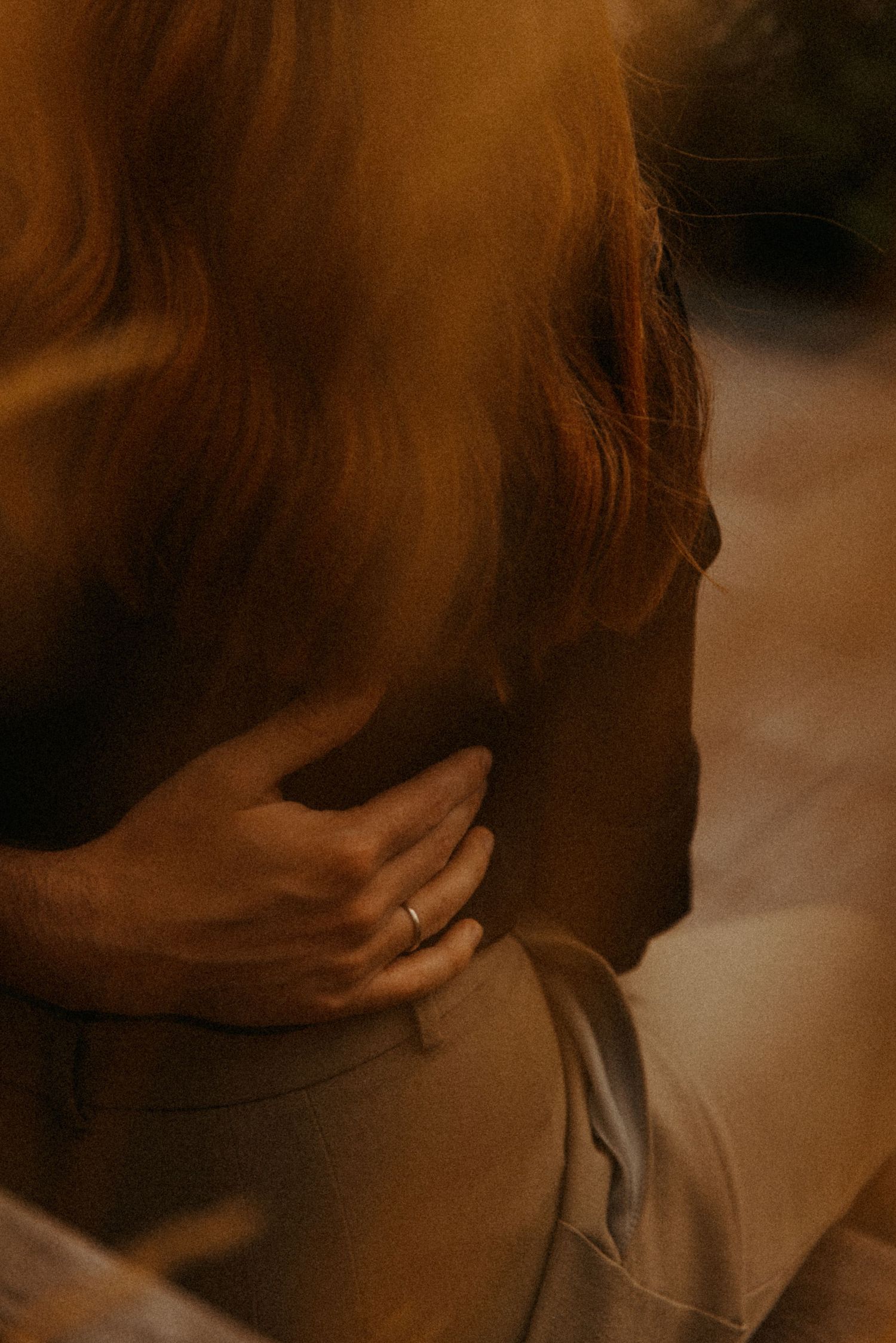 Close-up detail of a hand wearing an engagement ring against warm-toned background.