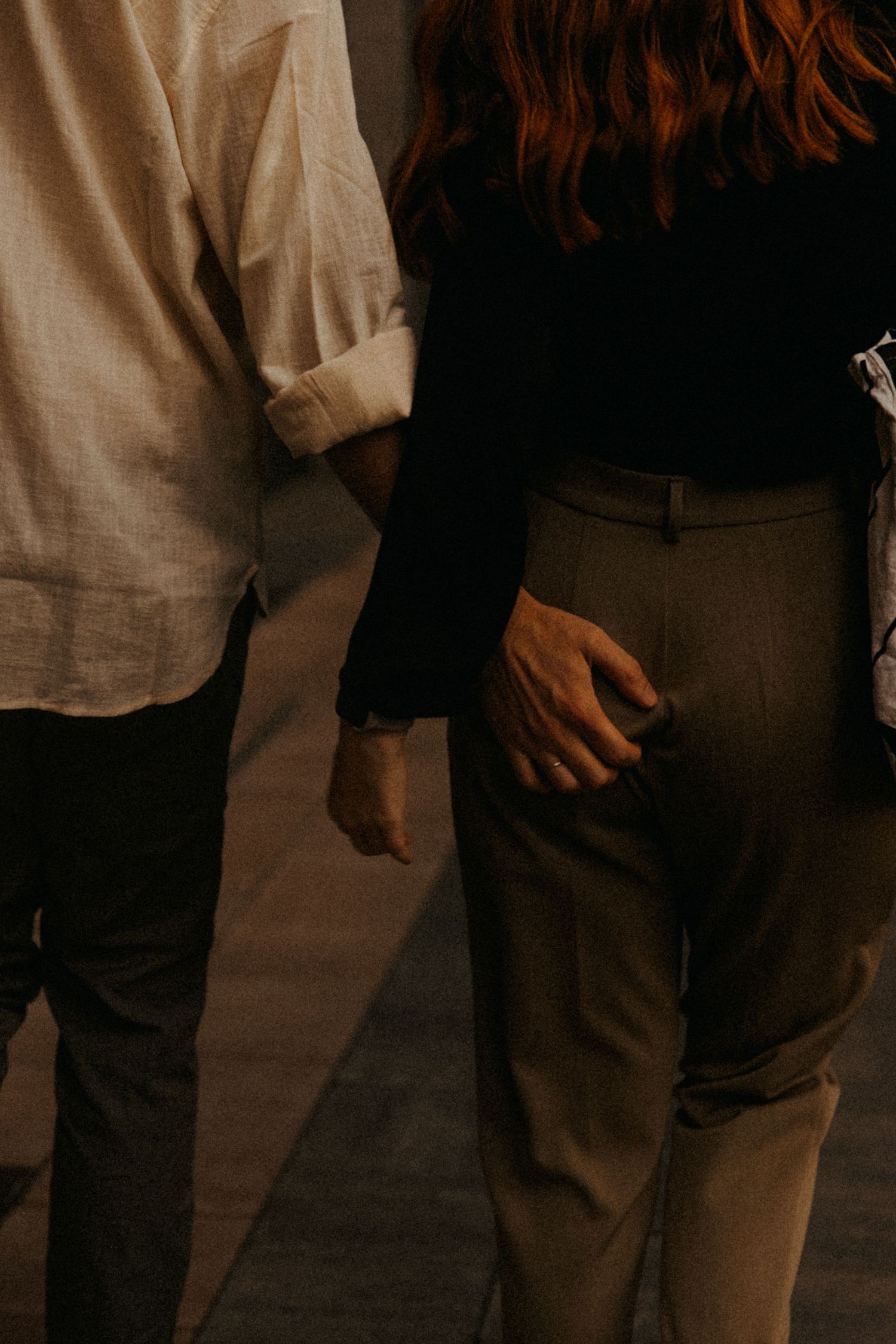 A couple stands close together in dim lighting, with one wearing a white shirt and the other in dark clothing.