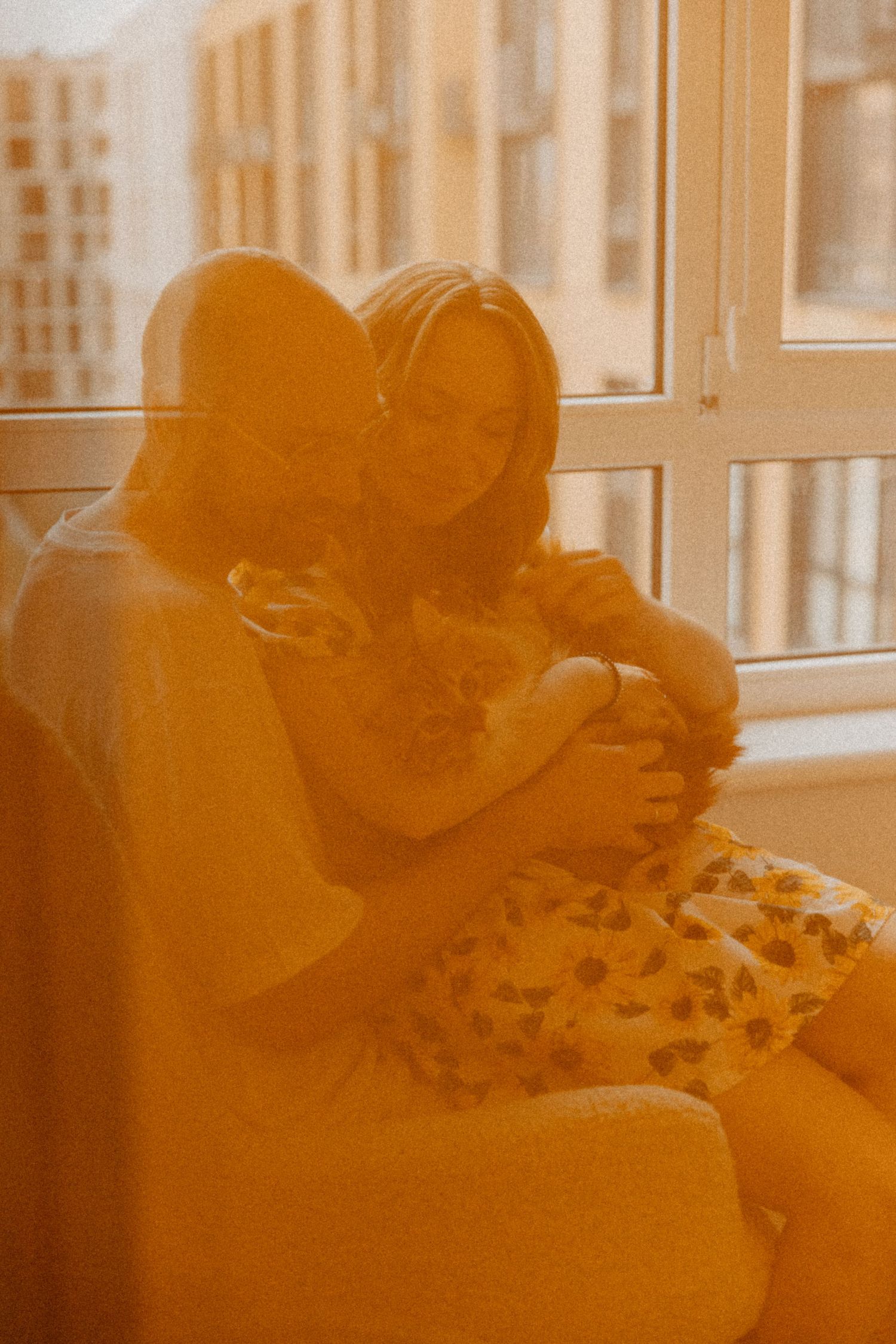 A warm-toned photograph of a tender embrace on a couch near a window.
