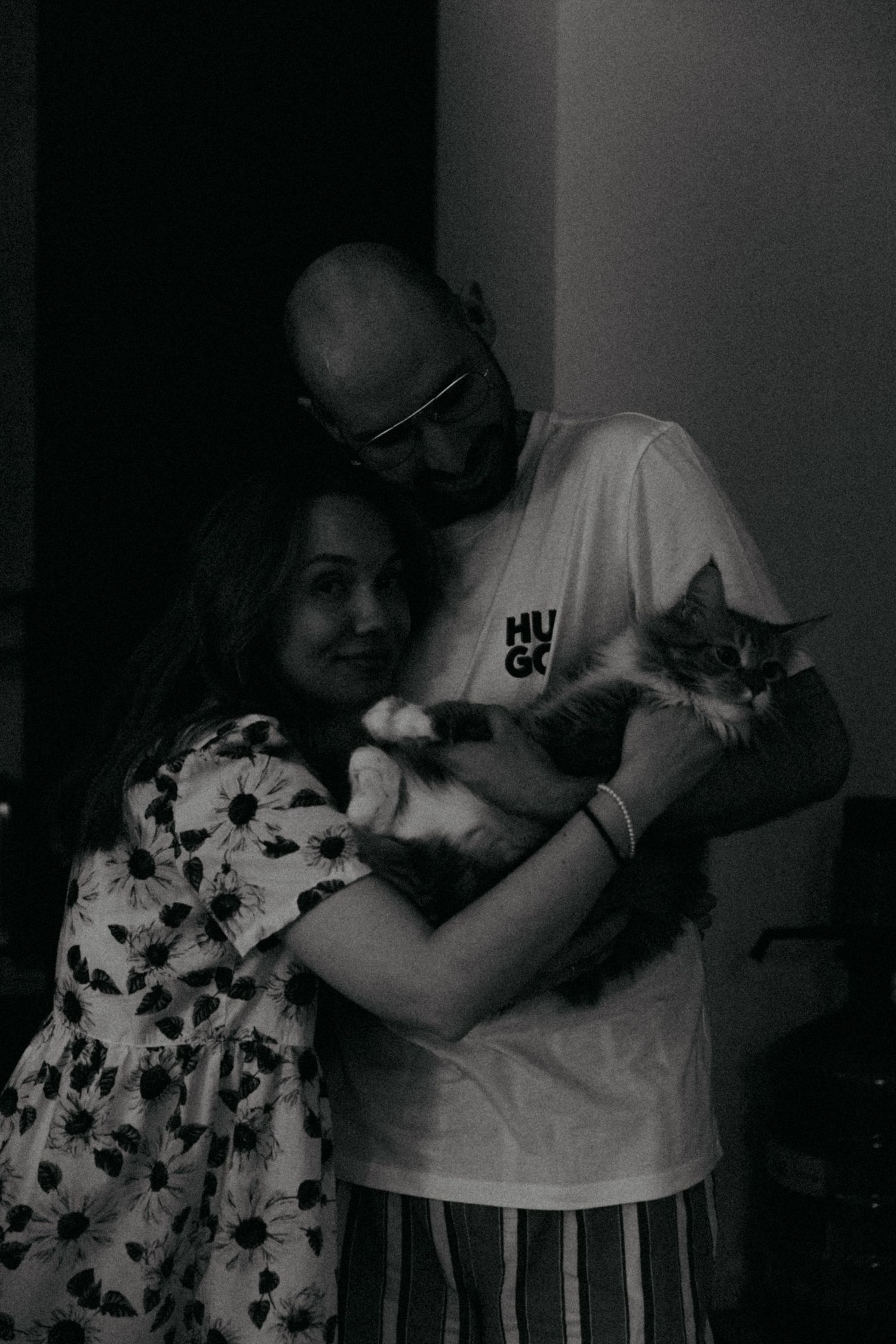 A couple holding a cat while posing together in black and white.