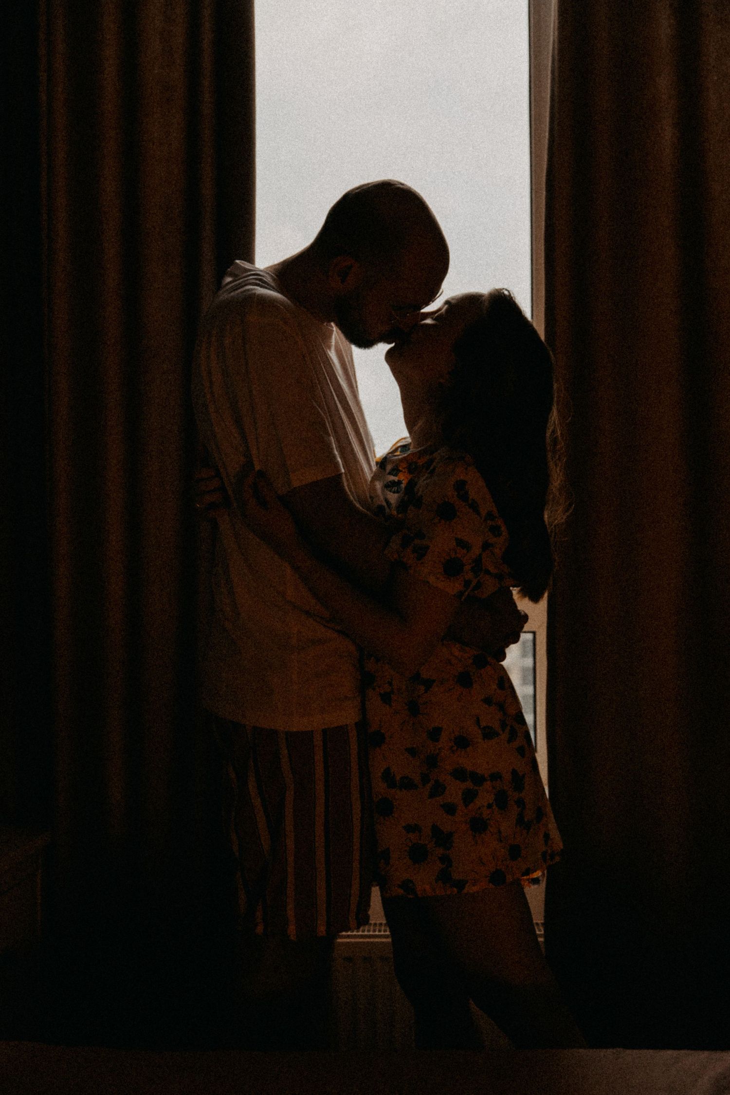 A silhouetted couple sharing an intimate moment between curtains.