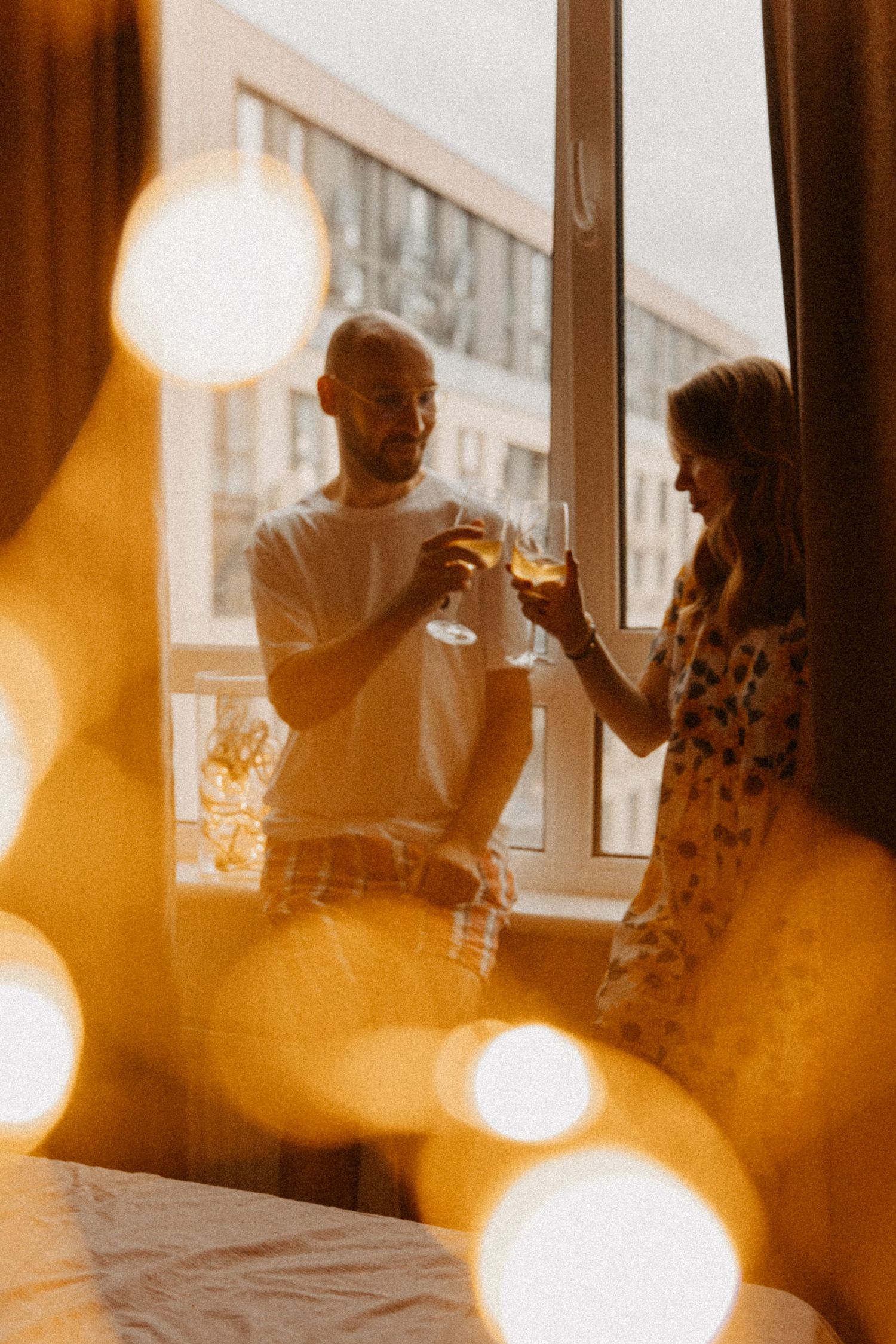 A couple toasting with wine glasses by a window at sunset.