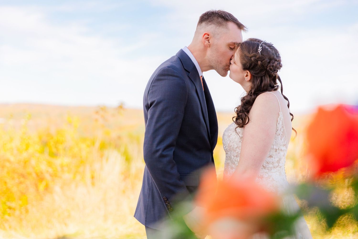 Romantic wedding portrait in golden field with red poppies in foreground.