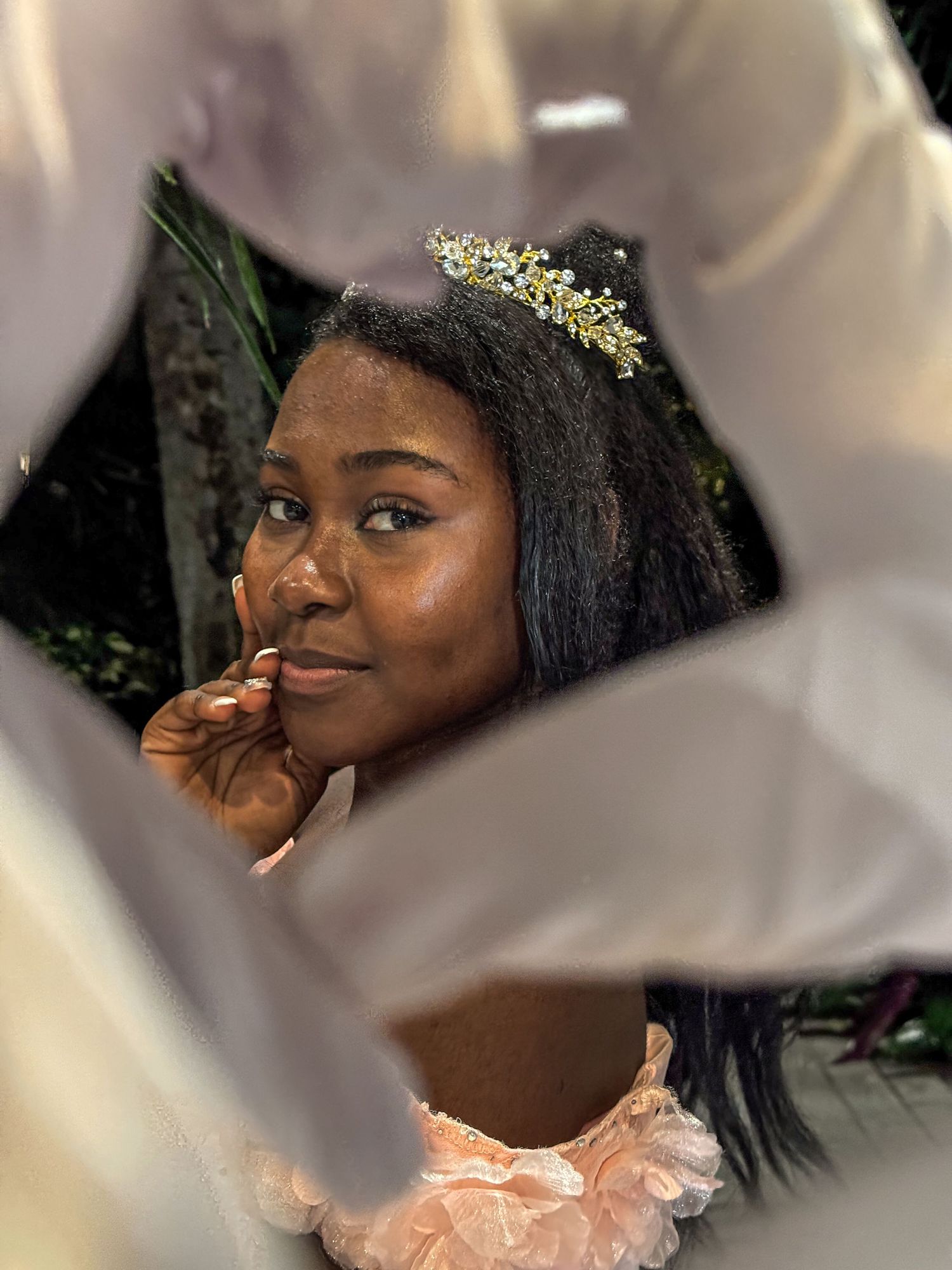 A dreamy portrait framed through fabric showing a gold tiara and peach dress.