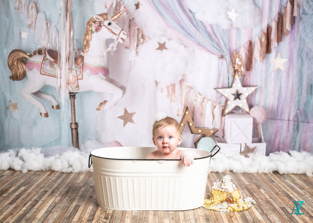 Baby peeking out of white basin in magical carousel-themed photo setup.