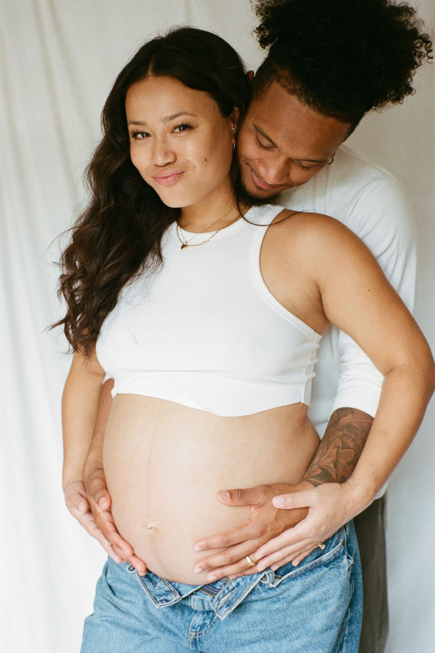 Sweet maternity photos capturing tender moments between expectant parents against white backdrop.
