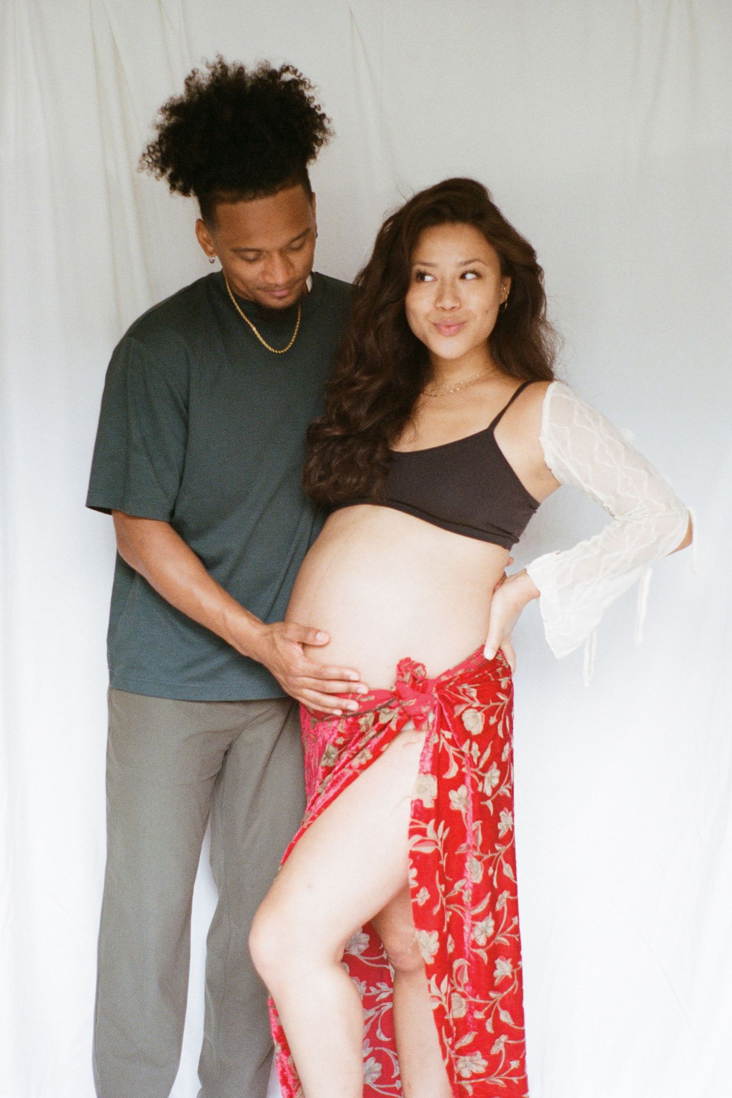 Couple stands together while showing off a growing baby bump in a candid photoshoot.