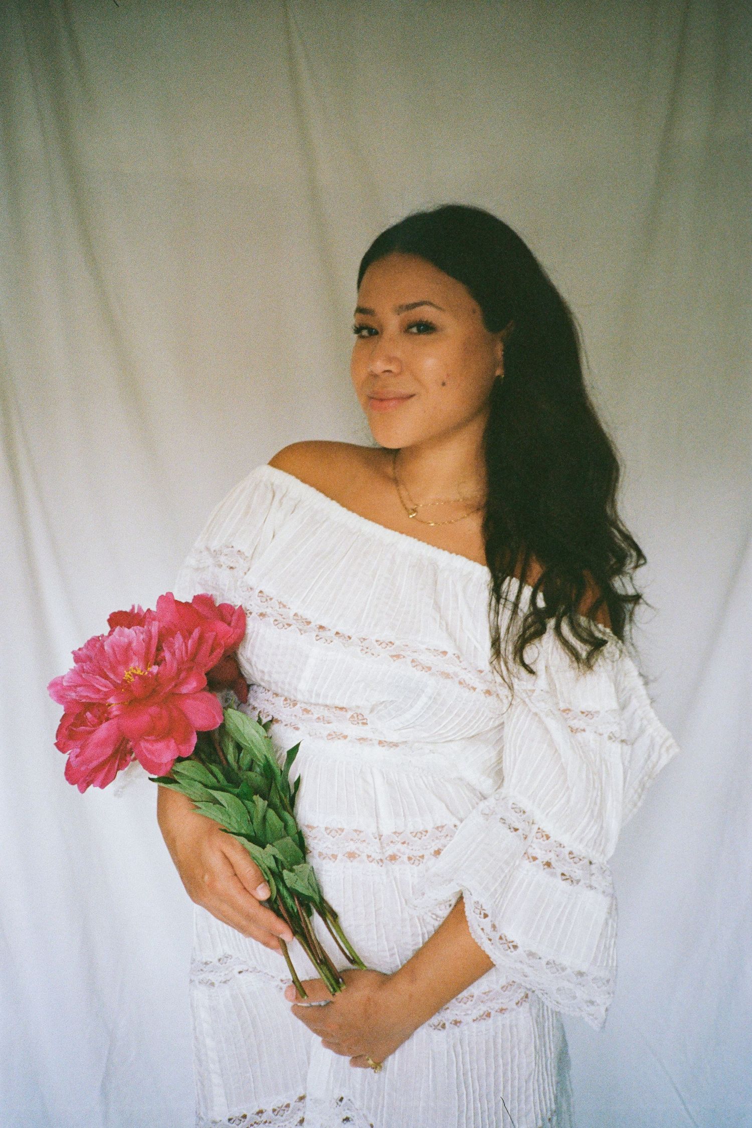 Woman in white lace dress poses with pink flowers during a photo session.