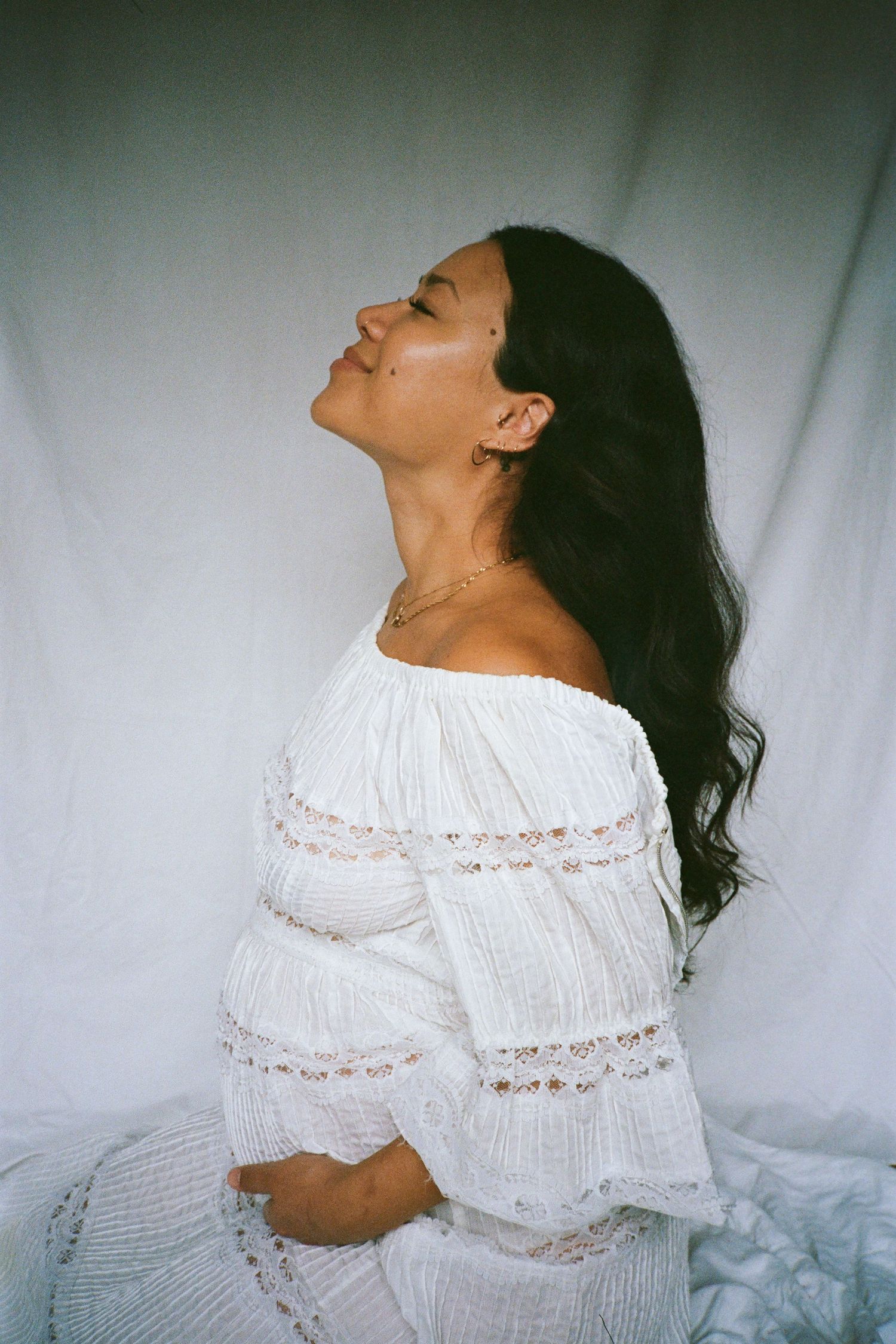 Woman in flowing white dress poses joyfully against white background.