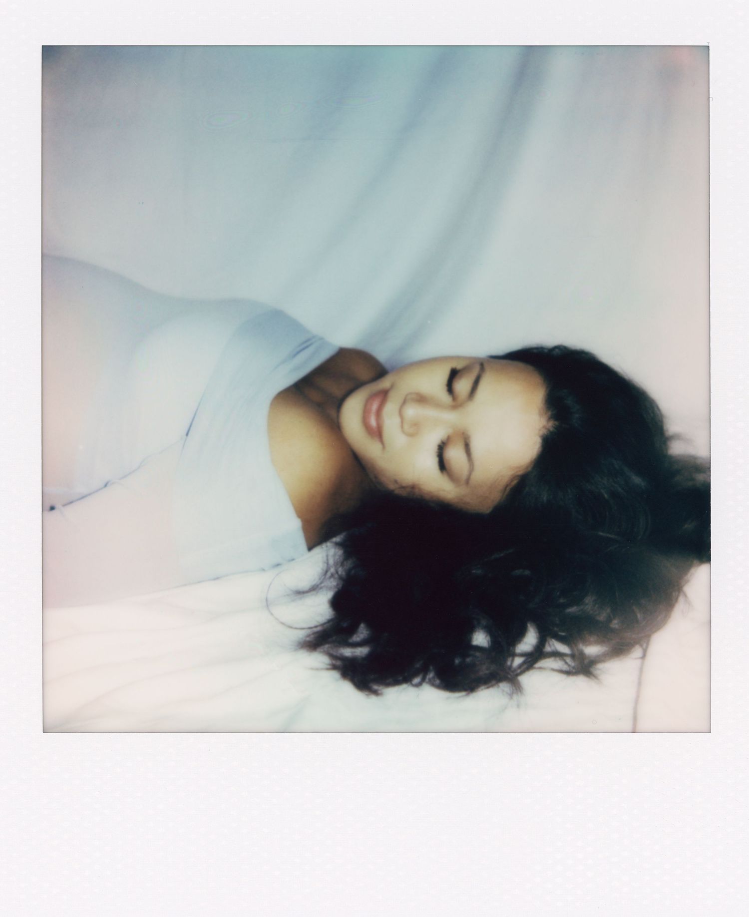 Dreamy polaroid portrait of a woman lying down with dark hair and white dress.