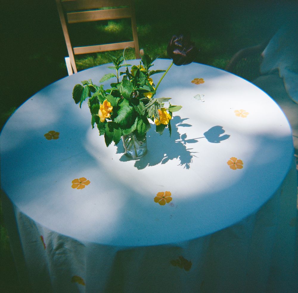 Yellow flowers in vase on round white table with floral pattern cloth.