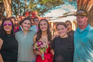 A group of people at an outdoor celebration with pink flowers and trees in the background.