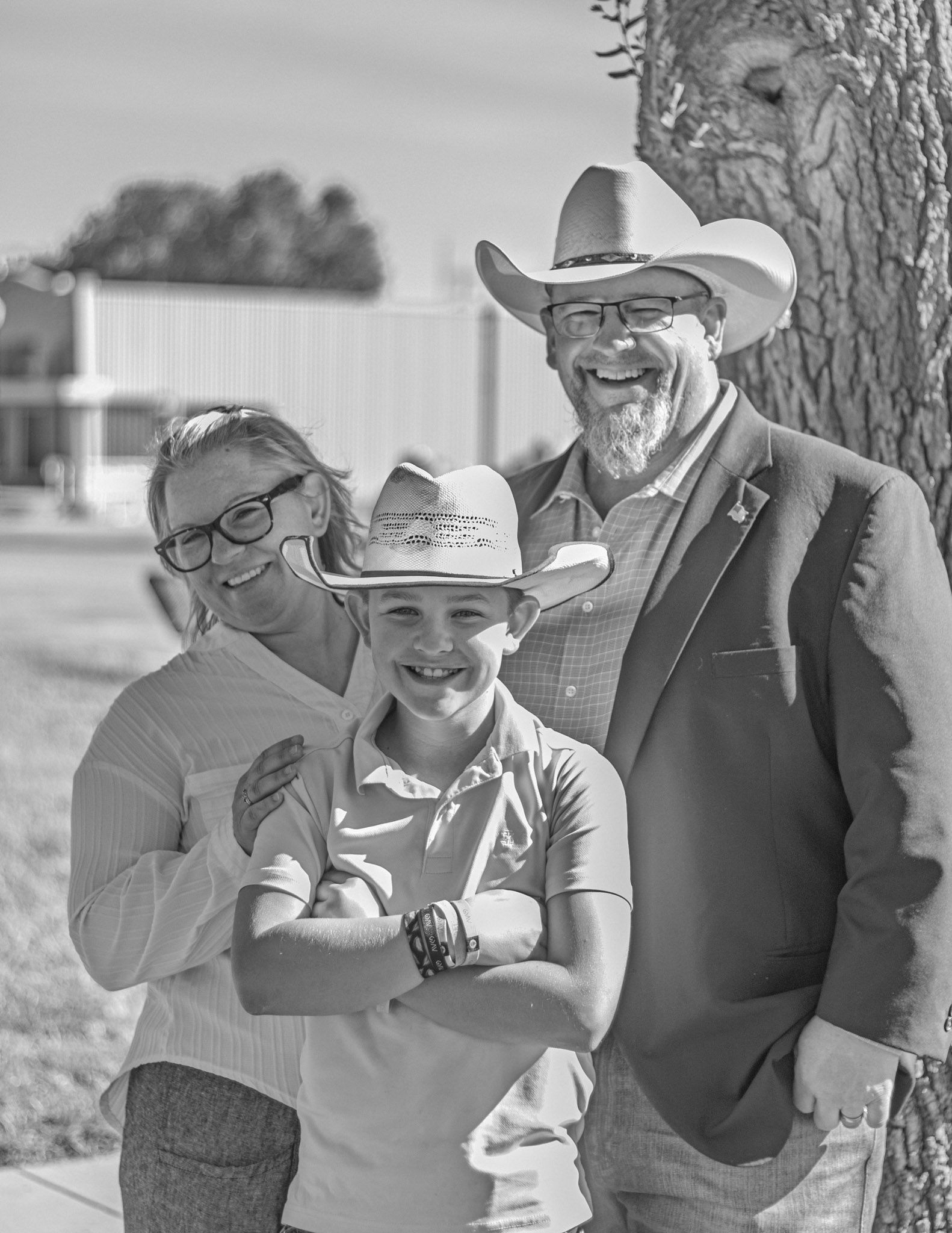 Black and white portrait of three people smiling together outdoors under a tree, all wearing cowboy hats.