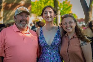 Three people standing close together outdoors at a social gathering on a sunny day.