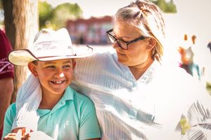 Two people outdoors sharing a lighthearted moment at a sunny outdoor event, one wearing a cowboy hat and teal shirt.