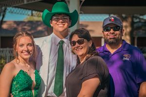 A group of four people posed together outdoors, with one wearing a green cowboy hat and tie and another in a purple shirt.