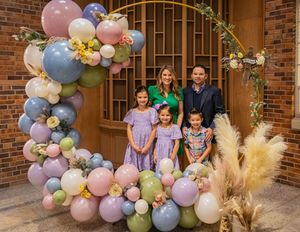 Outdoor portrait with decorative balloon arch in pastel pink and blue with dried pampas grass against brick entrance.