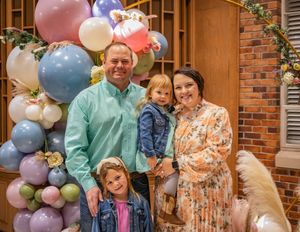 A group portrait in front of a brick wall with a pastel balloon arch featuring spring colors and floral decorations.