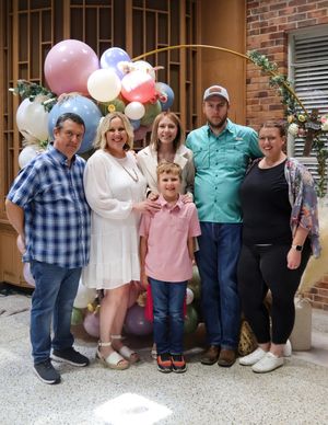 A group poses together by a brick wall with colorful balloons in pastel pink and white colors for a celebration.