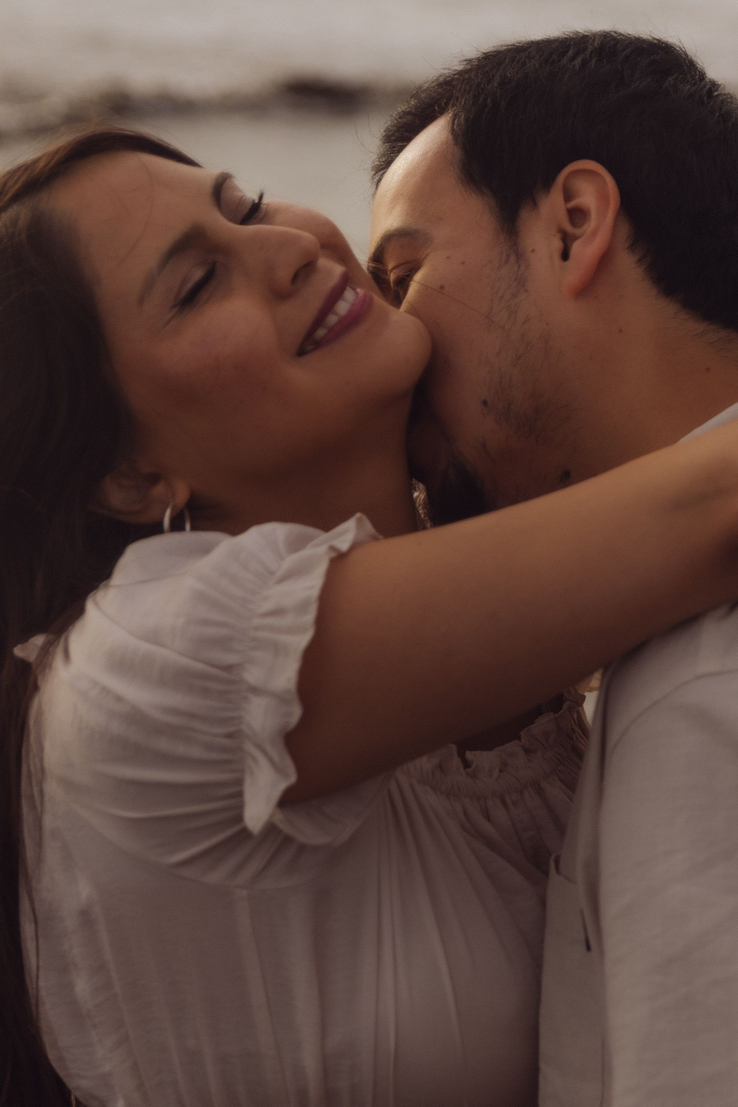 Man tenderly kissing smiling woman on cheek in a romantic close-up beach portrait.