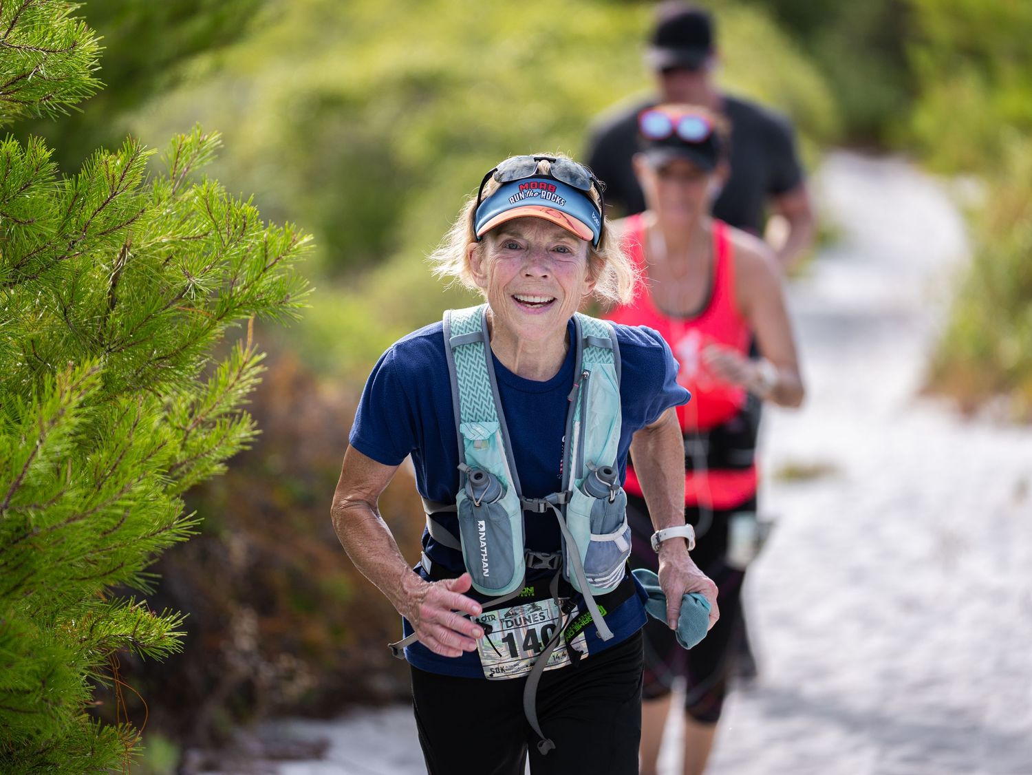 Trail runners traverse a scenic mountain path during an endurance race on a sunny day.