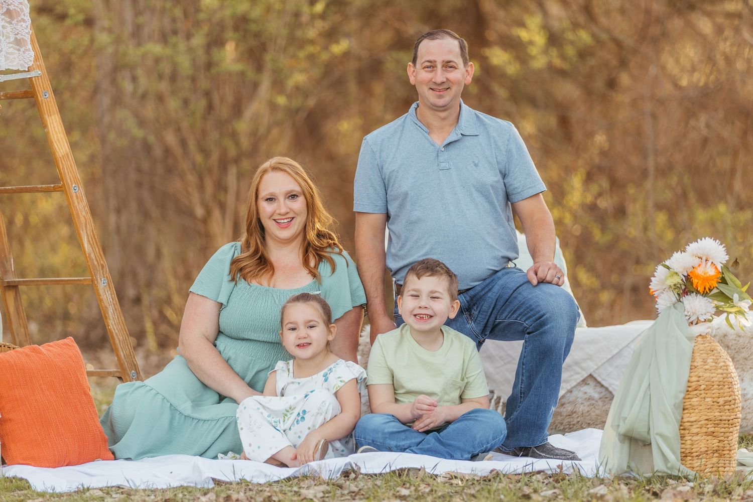 A family sits together on a picnic blanket during an autumn outdoor photo session with orange decor and flowers.