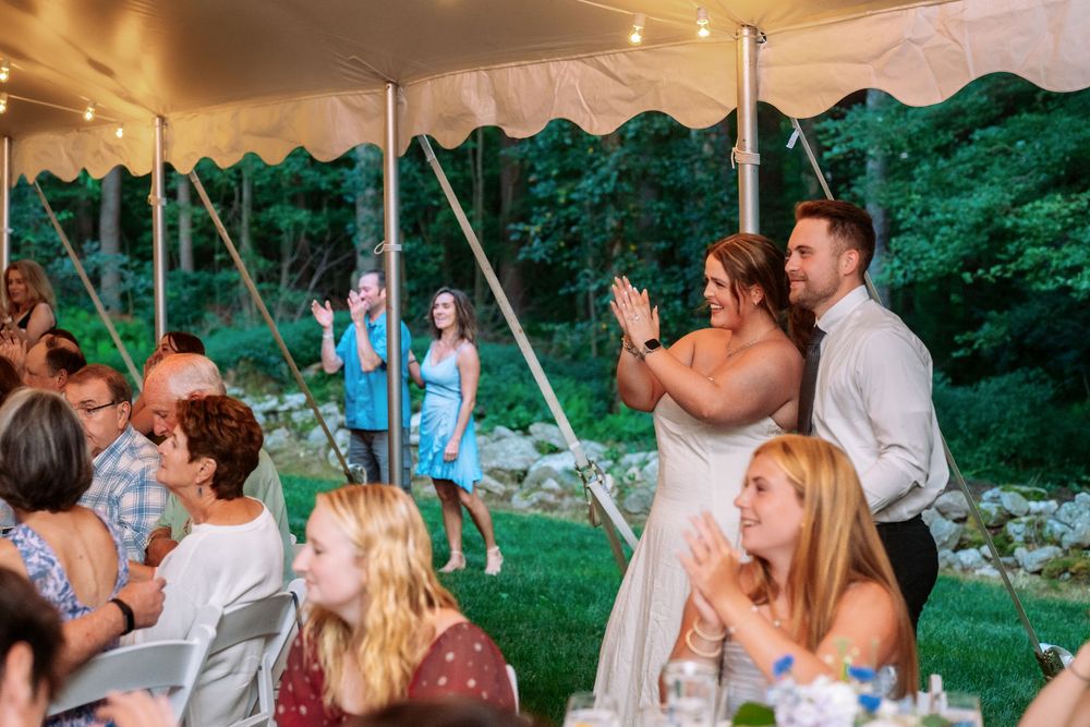 Guests celebrating under white tent at outdoor reception.