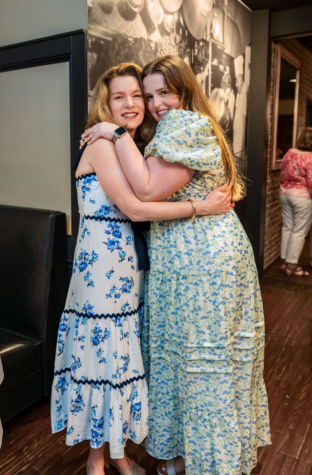 Friends in blue and floral dresses embracing during celebration.