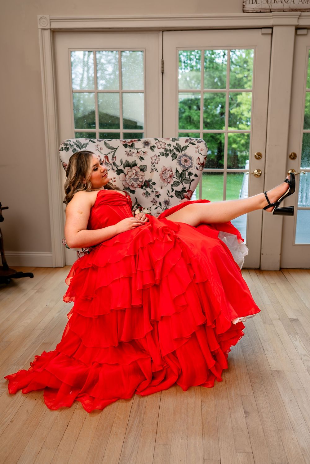 A dramatic red ruffled gown spreads across a hardwood floor near French doors and windows.