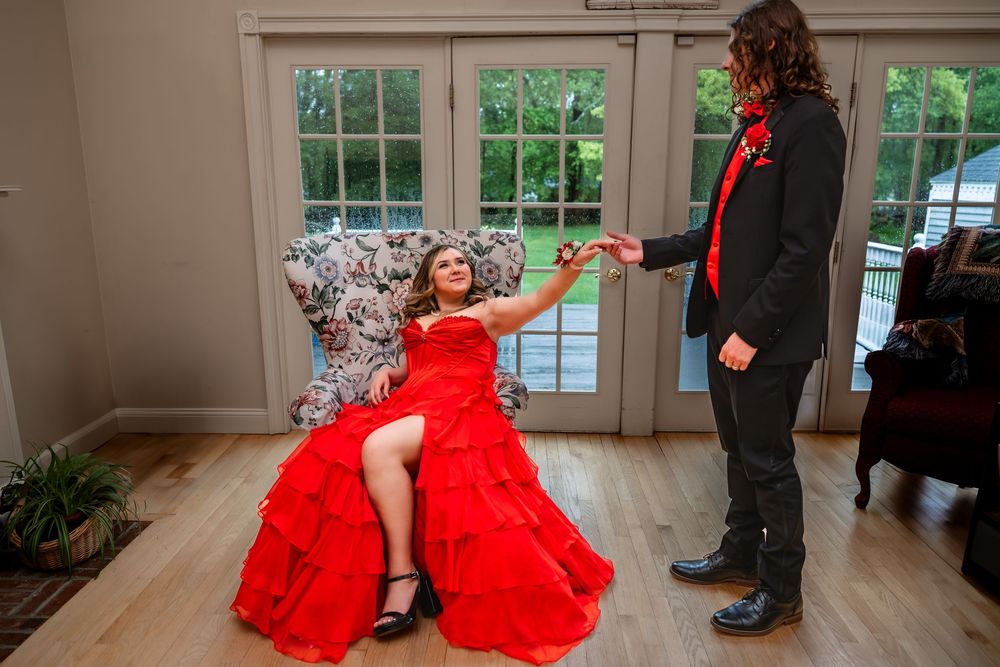A person in a stunning red ballgown poses dramatically on a wooden floor in an elegant room.