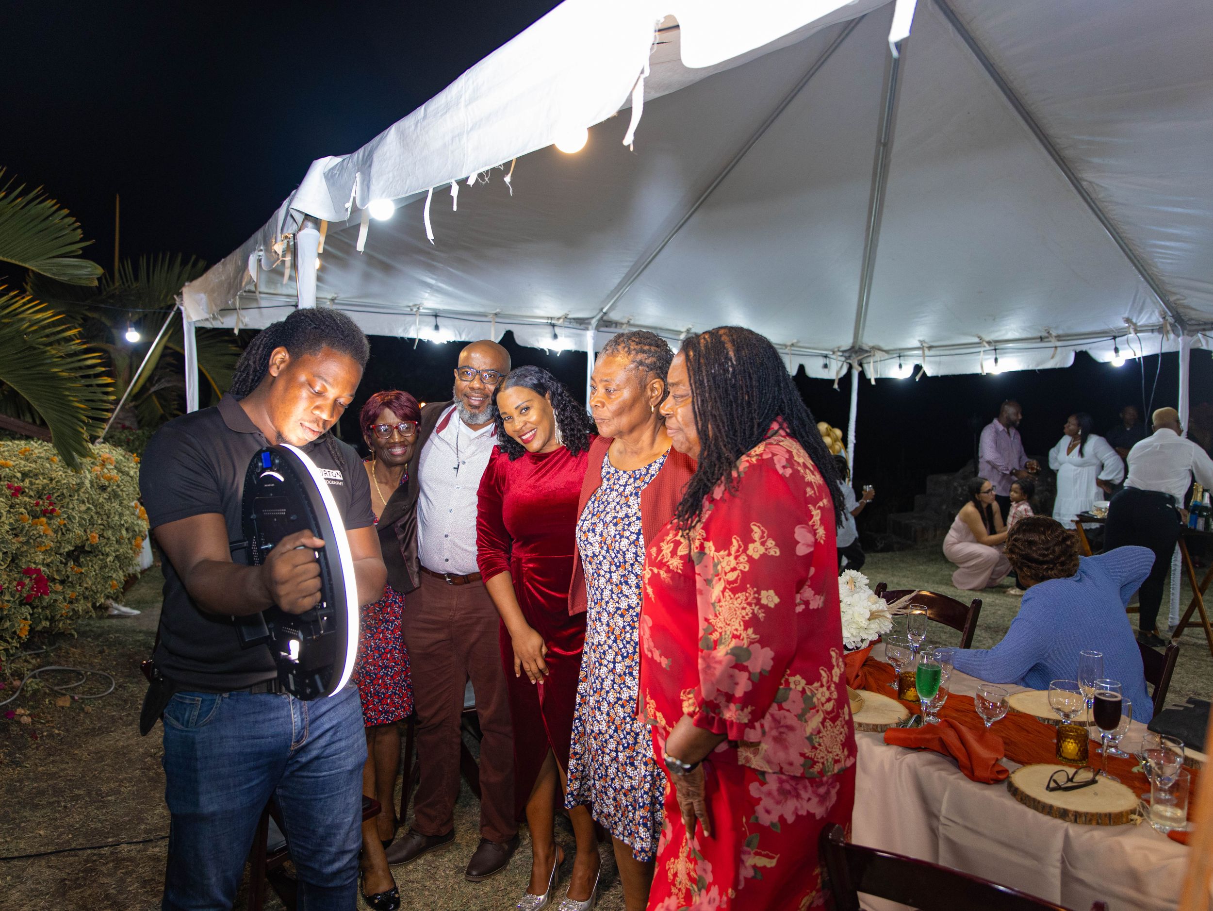 A group of people socializing under a white outdoor event tent during an evening gathering.