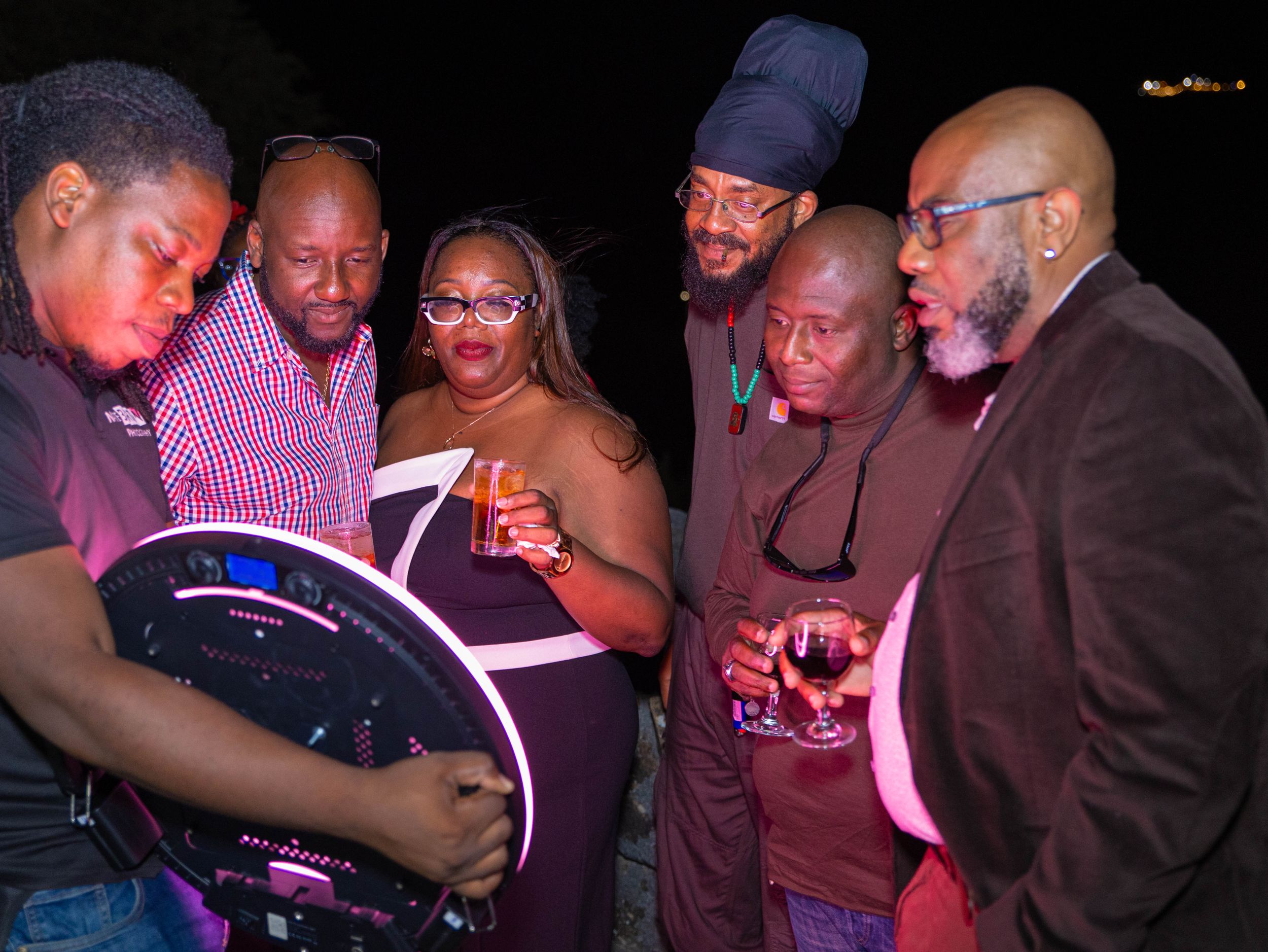 People gathered together looking at a book or document in a dimly lit setting with purple lighting.