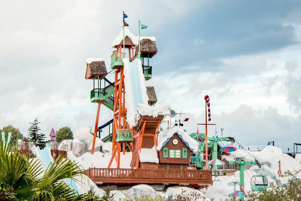 Theme park rides and attractions soar against a cloudy sky with colorful carnival decor visible in the scene.