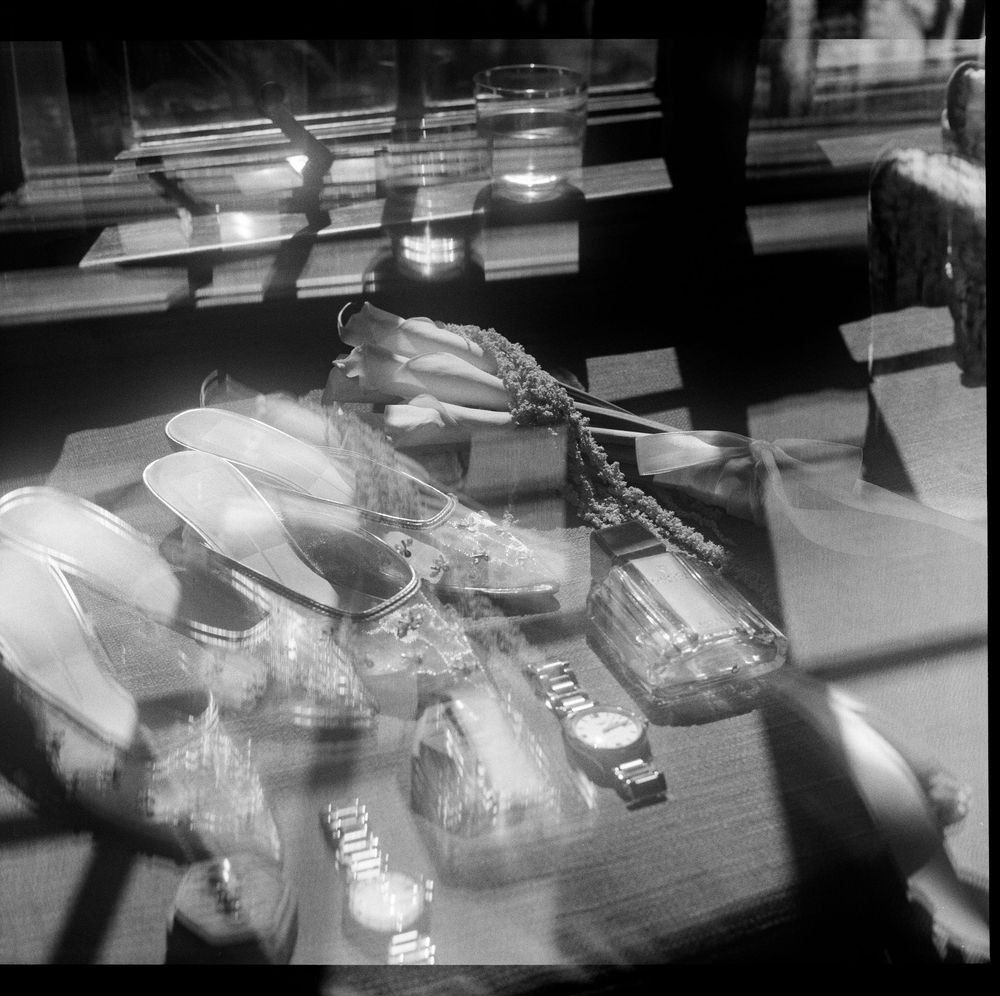 Black and white photo of a jewelry display case featuring watches, spoons, and accessories arranged on a sunlit surface.