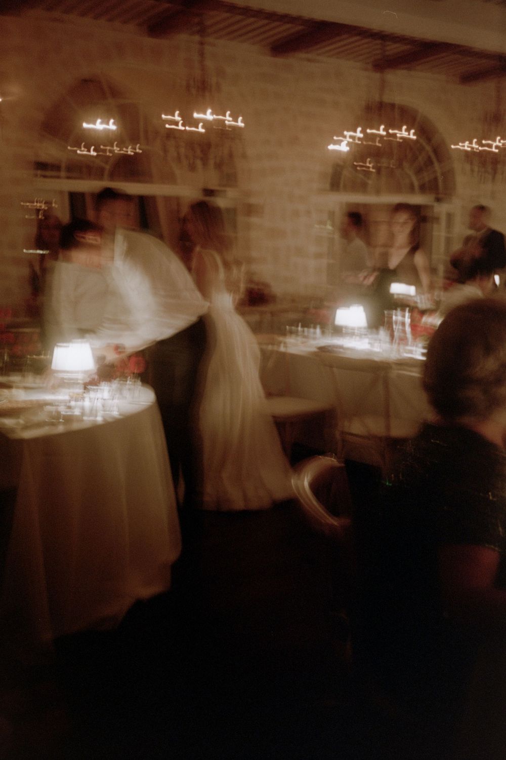 Blurry sepia-toned sequence of motion showing figures moving through a dimly lit room with chandeliers overhead.