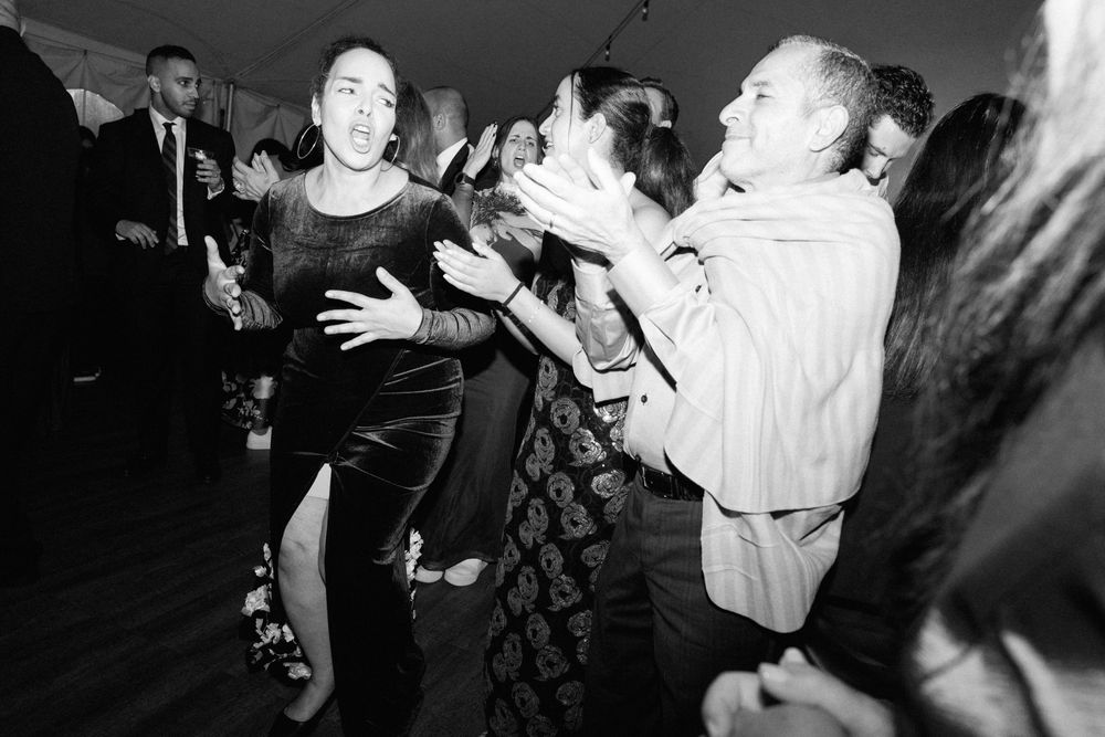 Black and white photo of guests dancing energetically at a lively wedding reception party.
