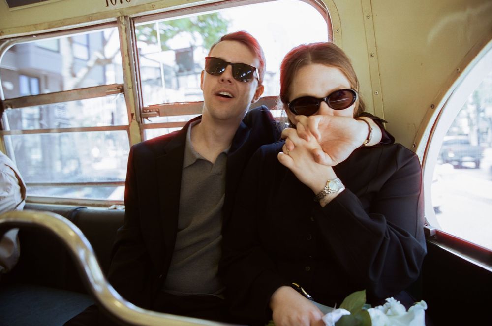 Two people smiling while sitting in the back seat of a vintage car in an urban setting.