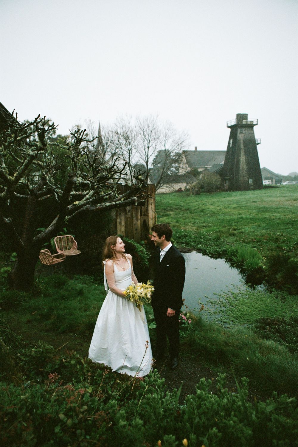 Scenic wedding portrait with a rustic lighthouse and stream in the background.