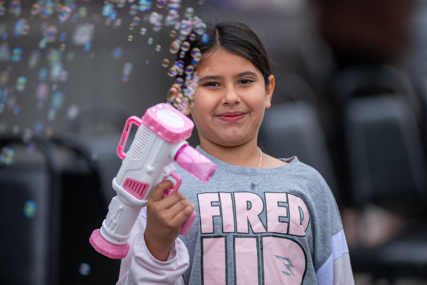 A young person holding up a pink toy water gun at an outdoor event.