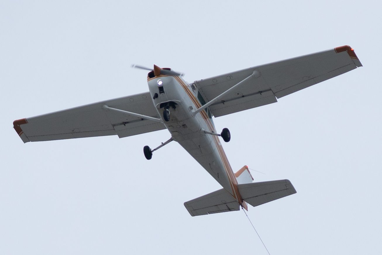 A small white aircraft flying overhead against a light blue sky.