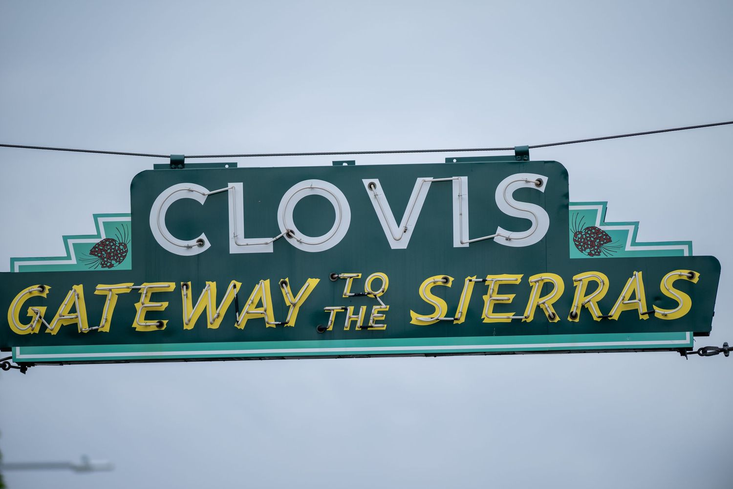 Green street signs reading 'Clovis Gateway to the Sierras' mounted on traffic light poles.