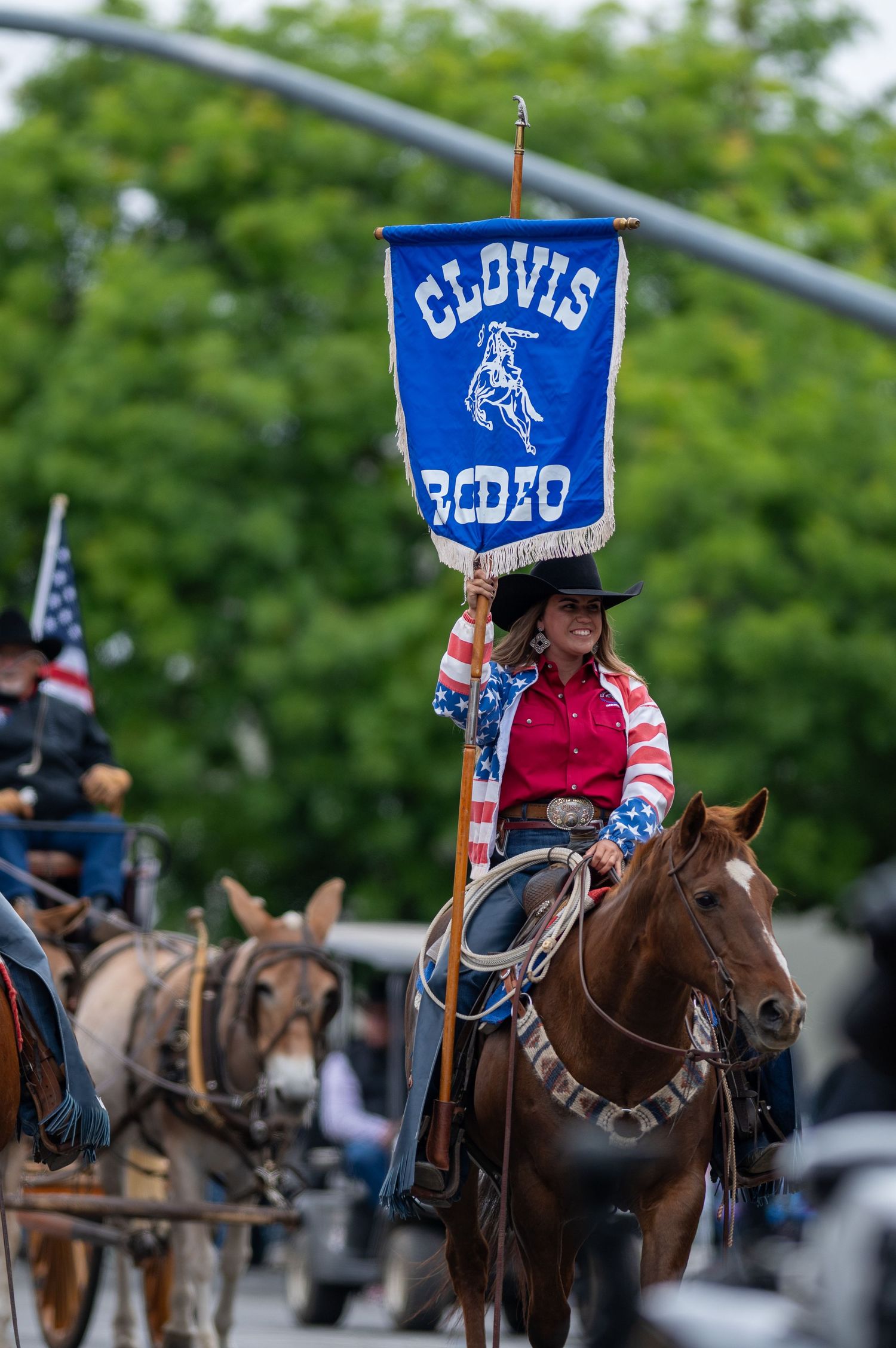 Equestrian participants carrying blue Clovis banners while riding horses in formation.
