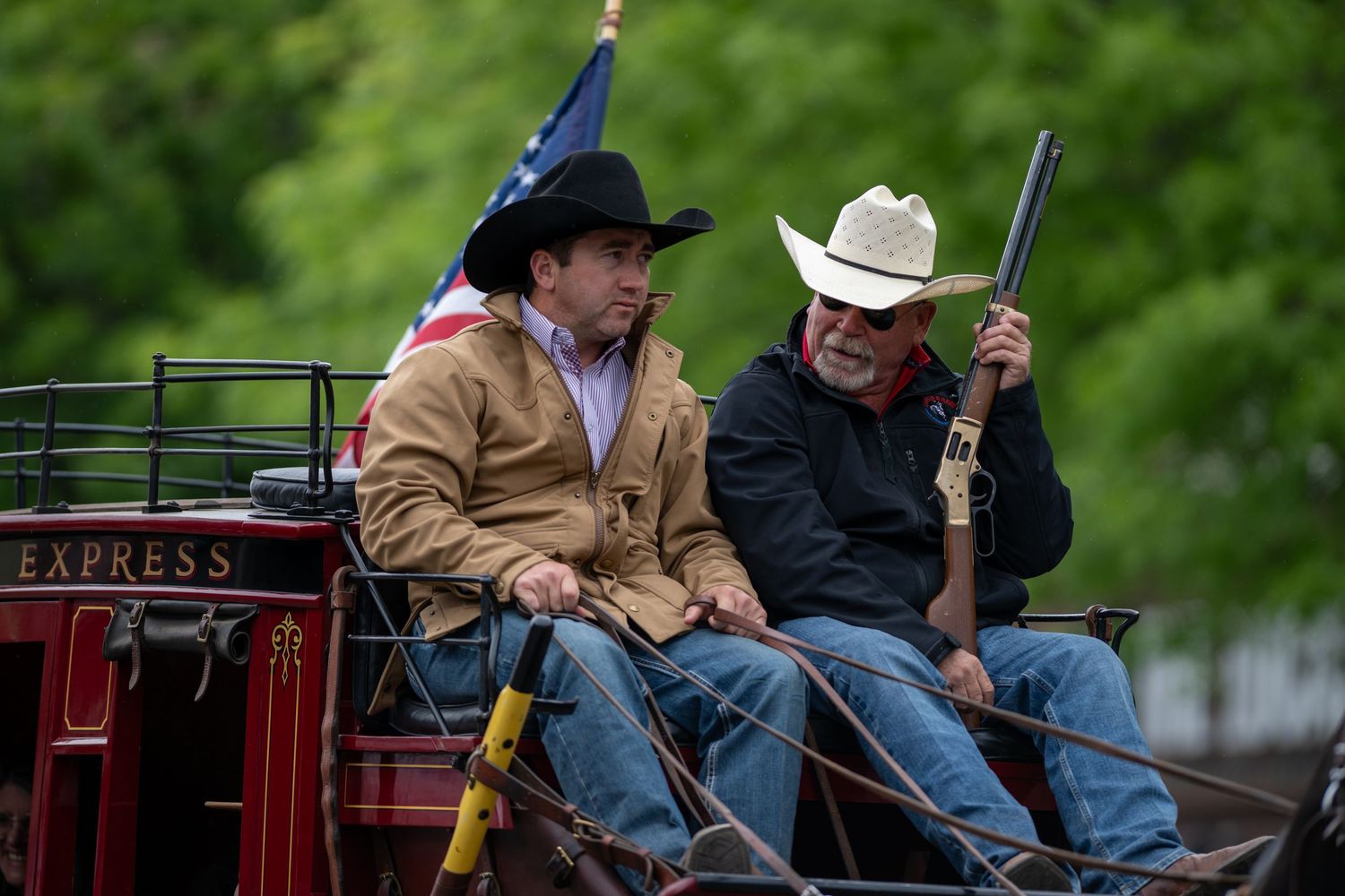 Cowboys riding on an antique farm equipment display in a small town parade.