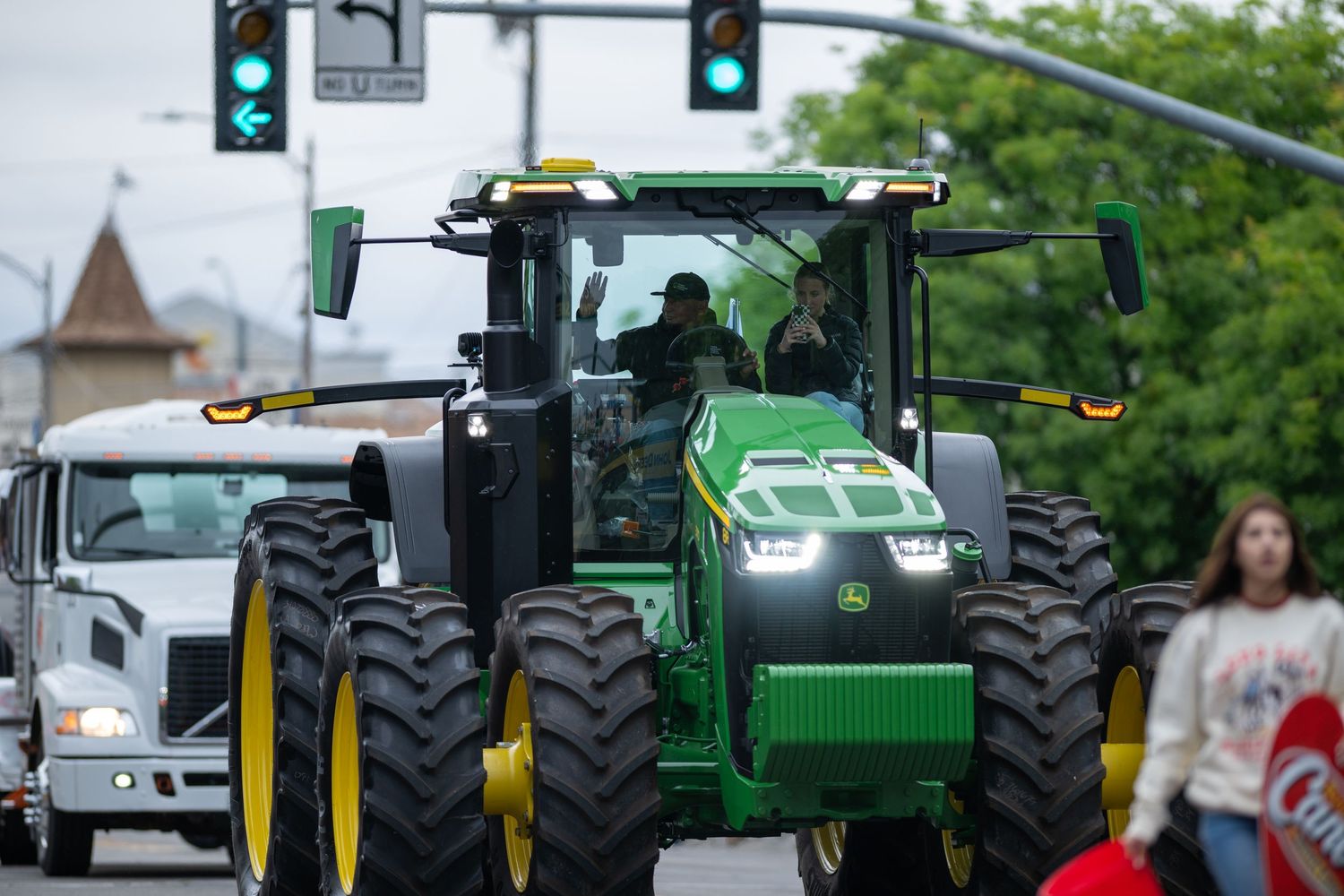 Large green John Deere tractors lined up in a parade formation on a city street.