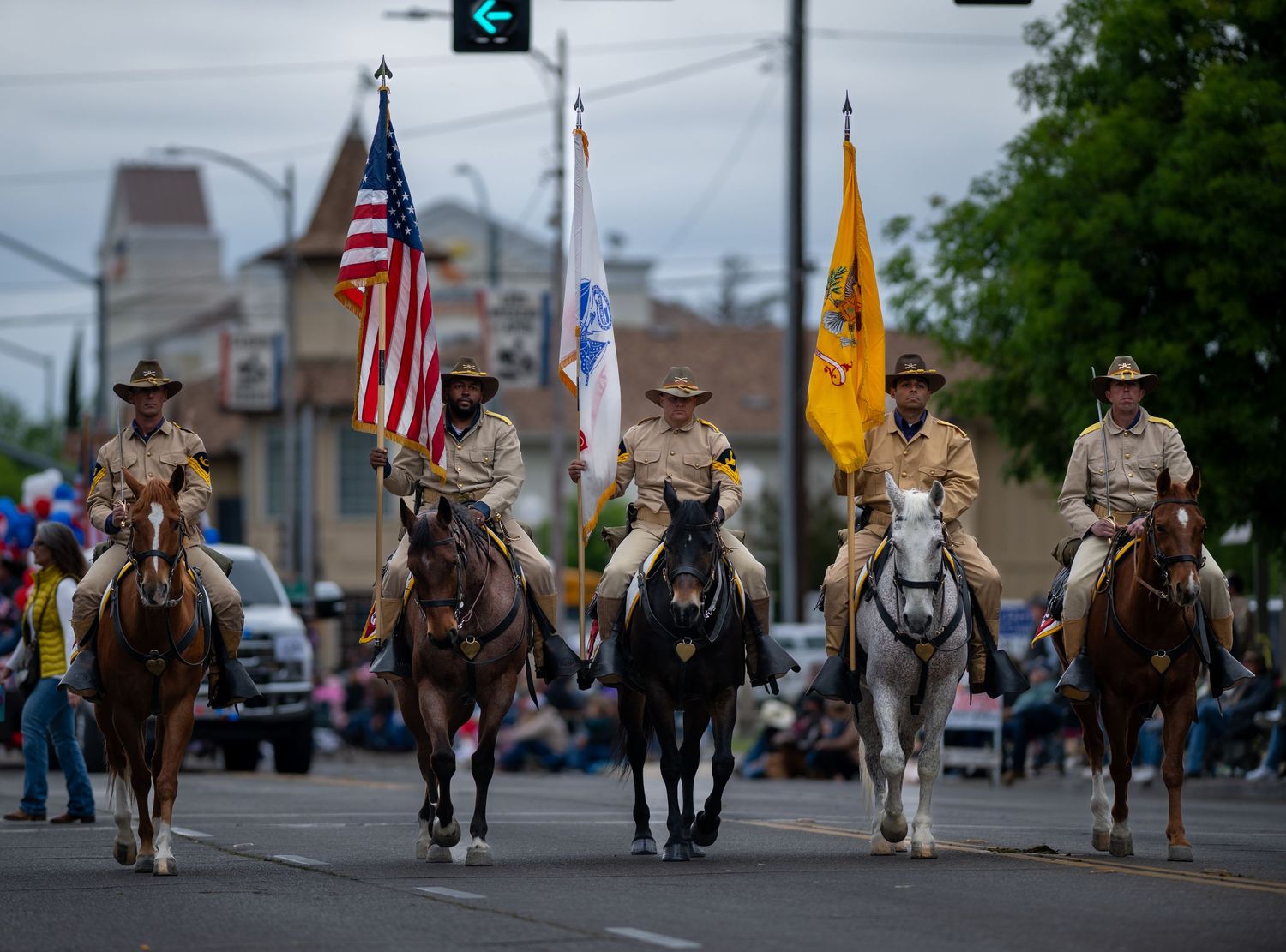 Horse riders in western attire parading down a street carrying American flags.