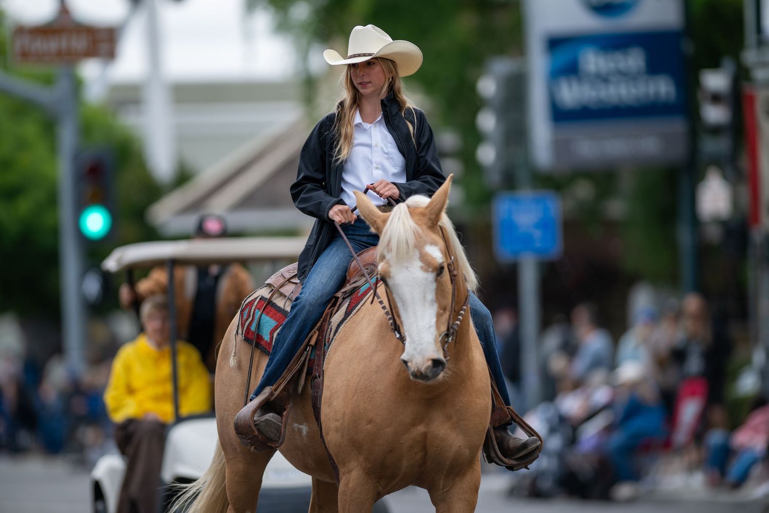 Horseback riders in western wear proceeding down a city street during a parade.