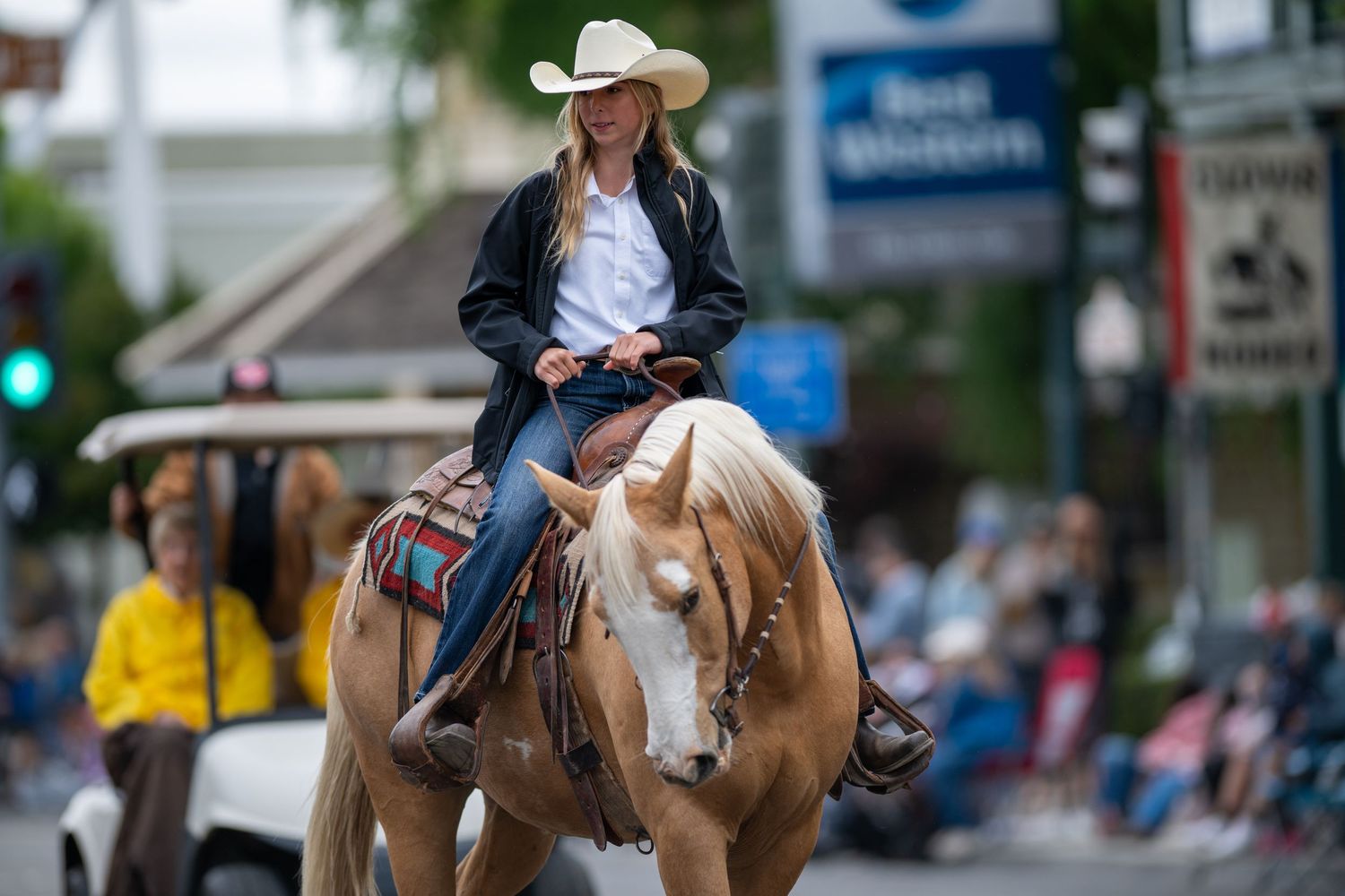 Mounted riders in cowboy hats guiding horses through a small town parade route.